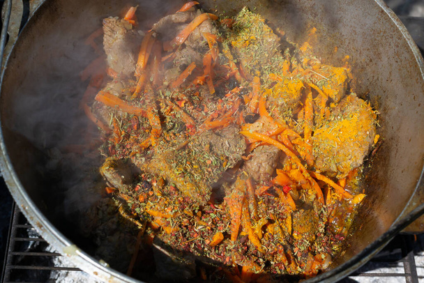 Cozinhar pilaf oriental tradicional em um caldeirão sobre um fogo. Pedaços cozidos de carne e cebolas e cenouras são cobertos com especiarias especiais e misturados. Zervak.. - Foto, Imagem