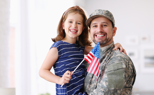 Portrait of happy american family father in military uniform and cute little girl daughter with flag of United States hugging and smiling at camera, male soldier dad reunited with family at home - Photo, Image