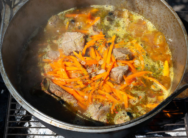 Cooking traditional oriental pilaf in a cauldron over a fire. Stewed pieces of meat and onions, carrots and spices are poured with boiling water and stewed for a while. Zervak. - Foto, Imagen