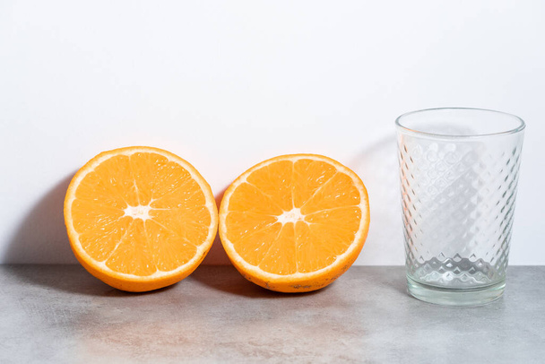 Coupe orange en deux et verre vide, sur fond gris avec dos blanc - Photo, image