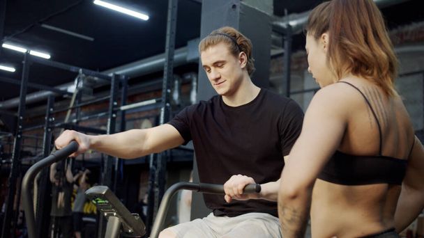 Сильный спортсмен тренируется на тренировочном цикле, и спортсменка разговаривает с ним - Фото, изображение