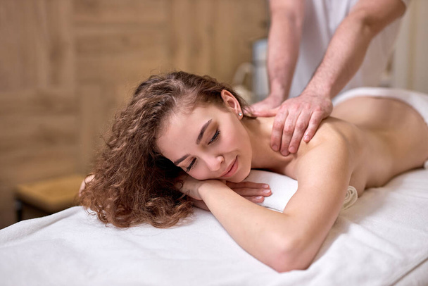 unrecognizable masseuses hands massaging female back, male kinesiologist massaging sensitive spinal column on back - Фото, зображення