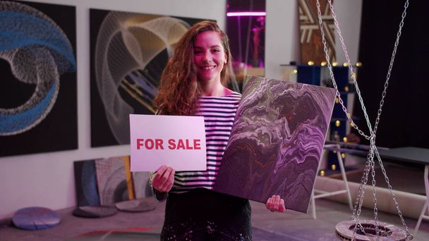 Молодая женщина показывает картину на продажу  - Фото, изображение