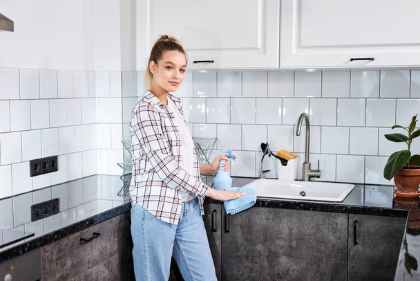 Woman cleaning kitchen with spray detergent and dish cloth, concept for hygiene - Fotó, kép