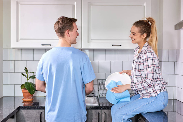Happy caucasian woman wiping dishes while husband washing at kitchen - Fotoğraf, Görsel
