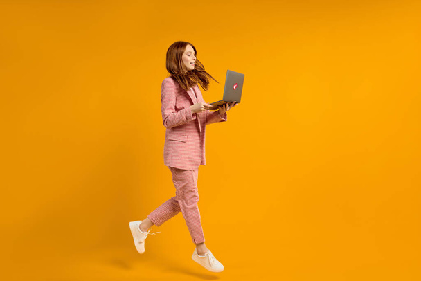 Excited jumping woman with laptop isolated on yellow background. Modern technologies - Foto, afbeelding