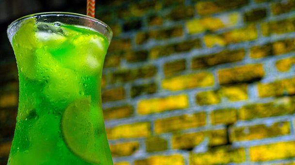 Green octail in a glass on a brick wall background. Green lemonade with ice. Summer fresh drink in a tall glass - Zdjęcie, obraz