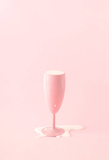 Roze champagneglas met gemorste melk. Roze achtergrond. - Foto, afbeelding