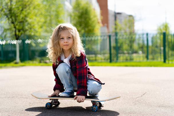 Little blonde girl on a skateboard in the city.  - Foto, afbeelding