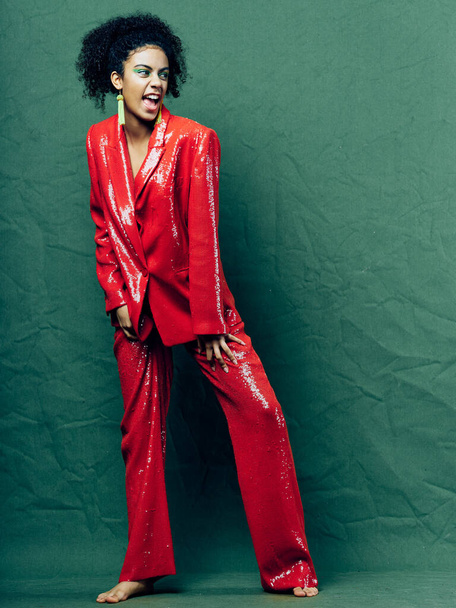 woman in a red suit on a green background in full growth curly hair model - Φωτογραφία, εικόνα