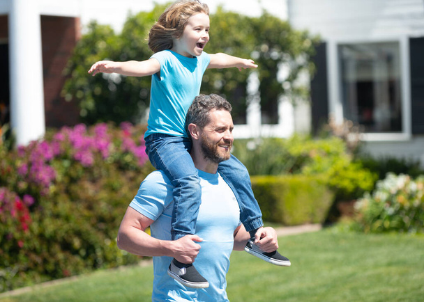 Happy man carry son kid sitting on fathers shoulders summer outdoors, piggy-back - Fotó, kép