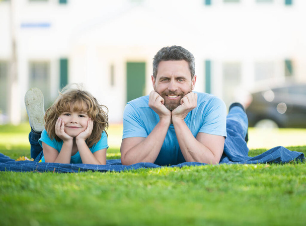Happy son child and father man enjoy relaxing on blanket on grass summer outdoors, family leisure - Foto, Imagem