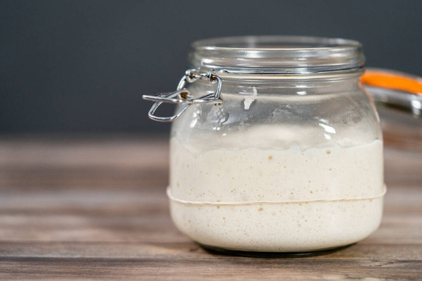 Feeding sourdough starter in a glass mason jar for baking artisan bread. - Fotoğraf, Görsel