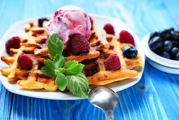 Belgian waffles with strawberry ice cream, fresh raspberries and mint, close up picture over blue background. - 写真・画像