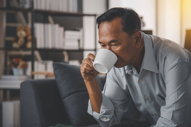 Az idősebb ázsiai apa melegen kávézik, mielőtt bemelegítene reggel az online munkában. A családi élet fogalma ma népszerű. - Fotó, kép