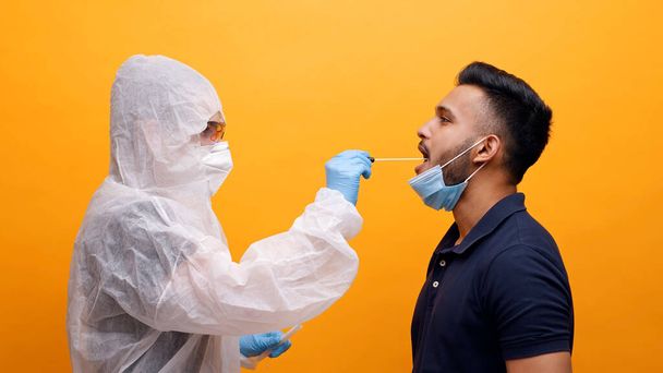 Pracownik służby zdrowia w kombinezonie ochronnym pobiera wymaz z jamy ustnej od potencjalnie zakażonego faceta - Zdjęcie, obraz