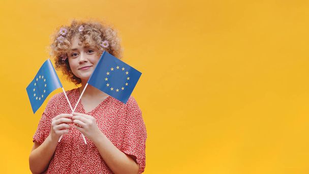 Houkutteleva nuori tyttö tilalla kaksi pientä Euroopan unionin lippua käsissään - Valokuva, kuva