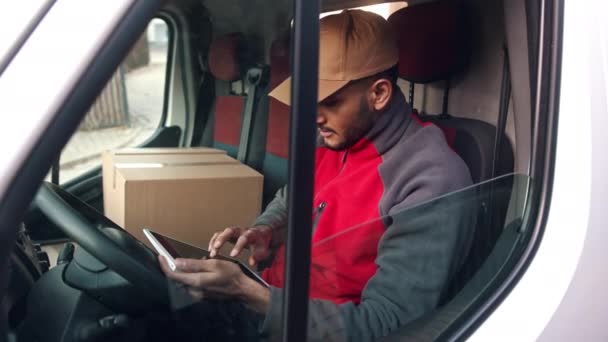 Ragazzo di consegna seduto nel furgone che cerca un indirizzo usando un pacchetto di compresse Consegna - Filmati, video
