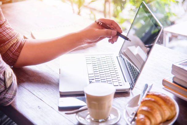 Un hombre usando un ordenador portátil con taza de café y pan en la mesa, buscando dirección e inspiración. - Foto, imagen