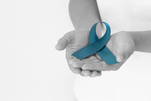 Hand holding teal color ribbon on white background with copy space. Ovarian Cancer Awareness, Gynecological, Uterine Cancer, Vulvar Cancer, Panic Disorder, Post Traumatic Stress Disorder (PTSD). - Photo, image