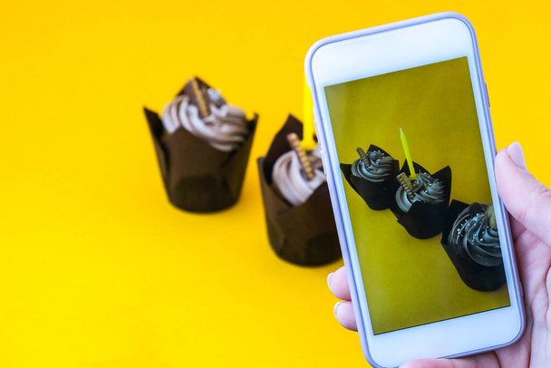 Female hands taking photo of Delicious chocolate cupcakes with cream on yellow background. Influencer Three chocolate muffin. Birthday cake party preparation. Homemade Chocolate Cupcake - Foto, immagini