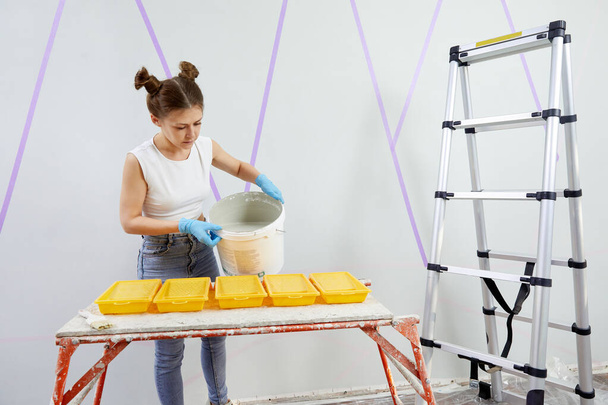 Молодая женщина заливает краску в пластиковый поднос для краски - Фото, изображение