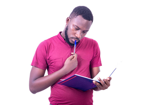 egy fiatal üzletember, aki pólót visel, fehér háttéren áll és naplót olvas, miközben gondolkodik.. - Fotó, kép