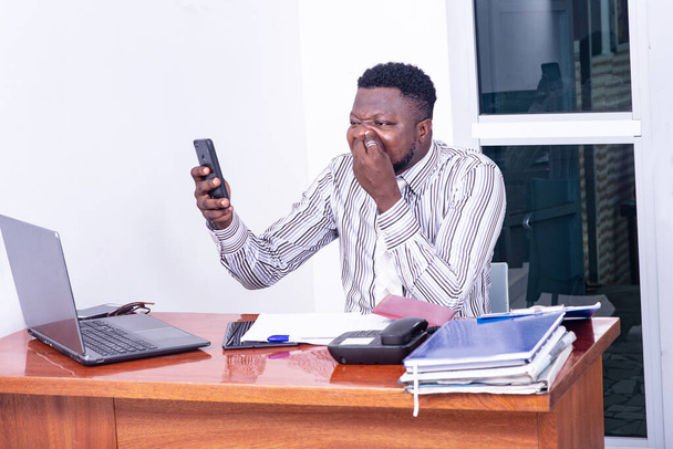 Ernsthafter erwachsener Geschäftsmann sitzt am Schreibtisch mit Blick auf den Laptop und telefoniert mit einem Handy. - Foto, Bild