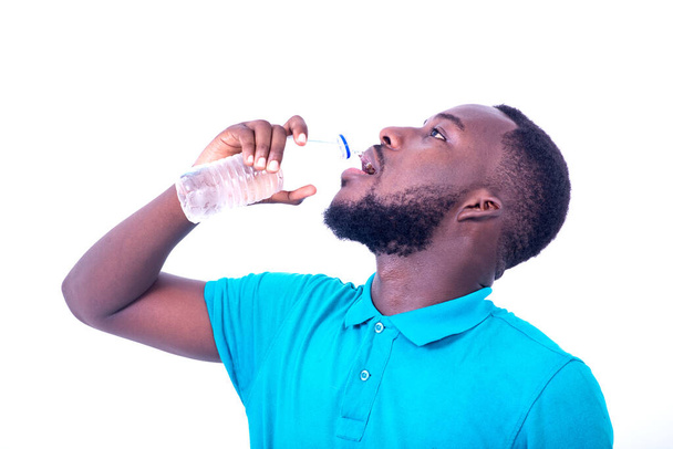 όμορφος διψασμένος νεαρός άνδρας φορώντας μπλε t-shirt πίνοντας μπουκάλι μεταλλικό νερό. - Φωτογραφία, εικόνα