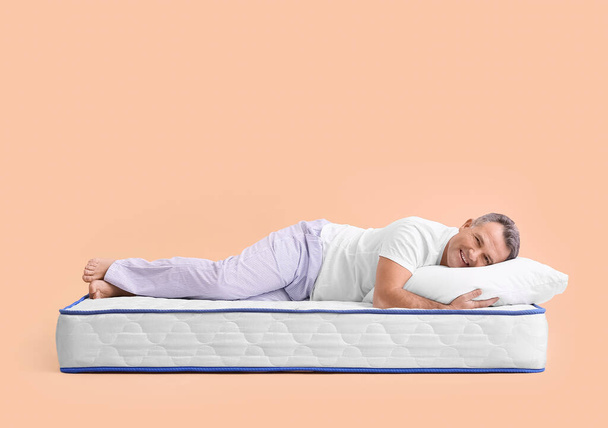 Mature man lying on soft mattress against color background - Photo, Image