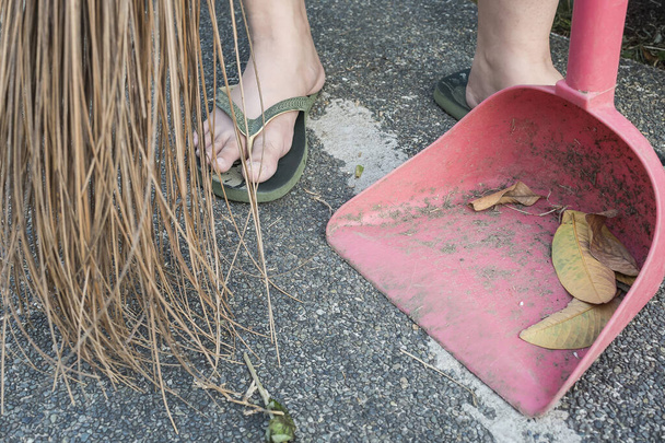 Sweeping leaves off the yard with walis tingting and dustpan. Walis tingting is a Philippine broom made from the thin midribs of palm leaves - Photo, Image
