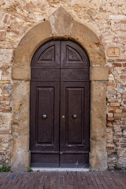 A vertical shot of an old arch door on a brick building in San Gimignano at Siena, Tuscany - 写真・画像