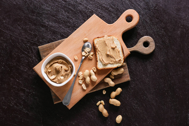 Bowl with tasty peanut butter and bread on dark background - Фото, изображение