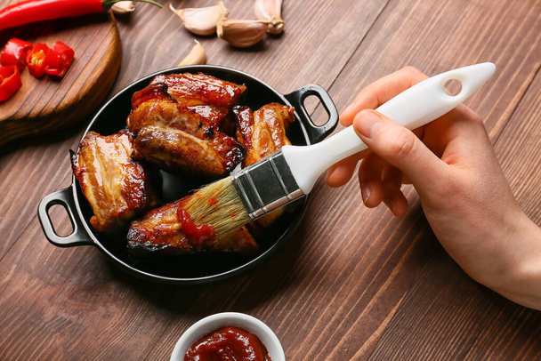 Woman spreading barbecue sauce on roasted pork on wooden background - Fotó, kép