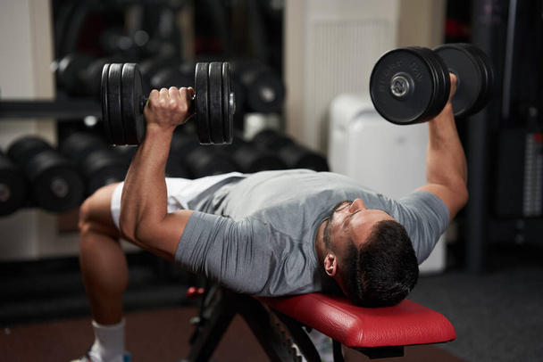 Young fitness man doing bench press with heavy dumbbells for chest workout - Foto, Bild