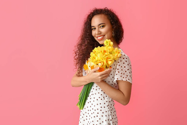 Beautiful young African-American woman with narcissus bouquet on color background - Photo, Image