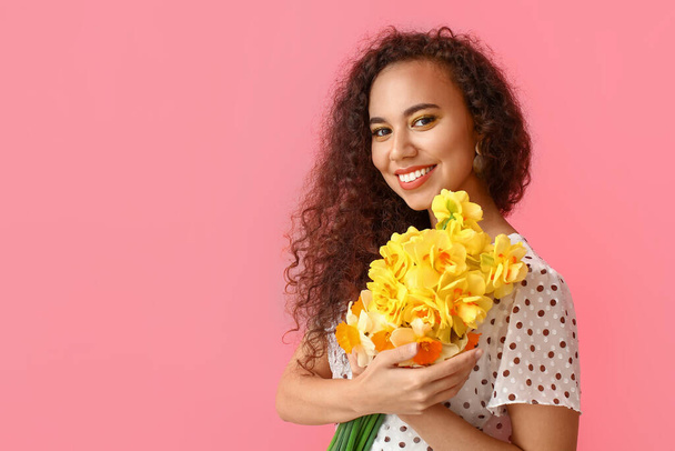 Beautiful young African-American woman with narcissus bouquet on color background - Fotoğraf, Görsel