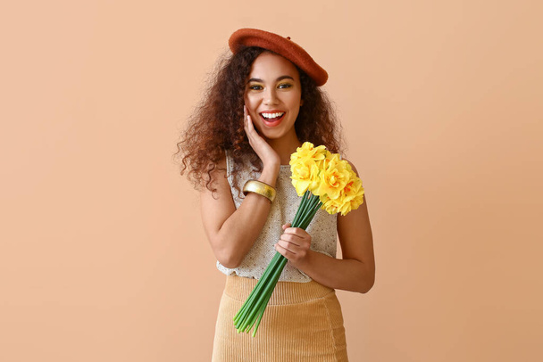 Beautiful young African-American woman with narcissus bouquet on color background - Foto, afbeelding