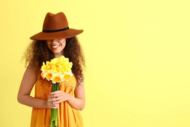 Beautiful young African-American woman with narcissus bouquet on color background - Foto, afbeelding