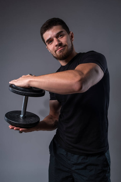 Smiling athletic young man with dumbbell in hands - Foto, imagen