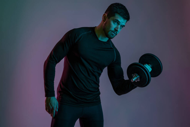 Handsome athletic guy performing arms exercises with dumbbell - Photo, Image