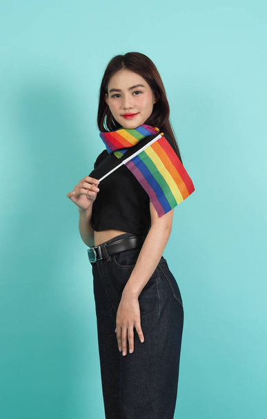 LGBTQ meisje en trots vlag. Sexy lesbisch meisje en LGBTQ vlag staan. blauw groene achtergrond. Aziatische LGBTQ vrouw met regenboog sjaal op de hals. Energiek, vrolijk. LGBTQ concept. LGBTQA + Pride Maand. - Foto, afbeelding