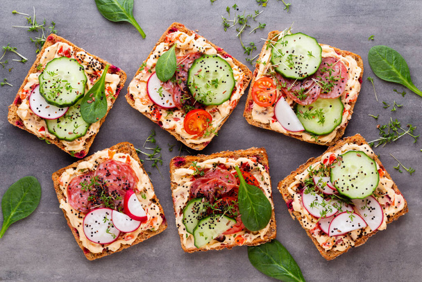 Sandwiches with cream cheese, vegetables and salami. Sandwiches with cucumber, radish, tomatoes, salami on a gray background, top view. Flat lay. - Fotografie, Obrázek