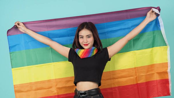 Dziewczyna LGBTQ i flaga dumy. Seksowna lesbijka i flaga LGBTQ na stojąco. niebieskie zielone tło. Azjatka LGBTQ z tęczowym szalikiem na szyi. Energicznie wesoły. Koncepcja LGBTQ. LGBTQA + Miesiąc Pychy. - Zdjęcie, obraz