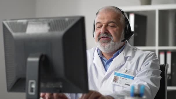 Muž praktický lékař v bílém plášti sedí za stolem v ordinaci lékařů a rolování počítačové myši při čtení pacientů zdravotní anamnézy - Záběry, video