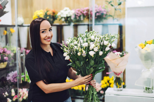 Ritratto di una fiorista con un mazzo di rose bianche tra le mani in un negozio di fiori - Foto, immagini