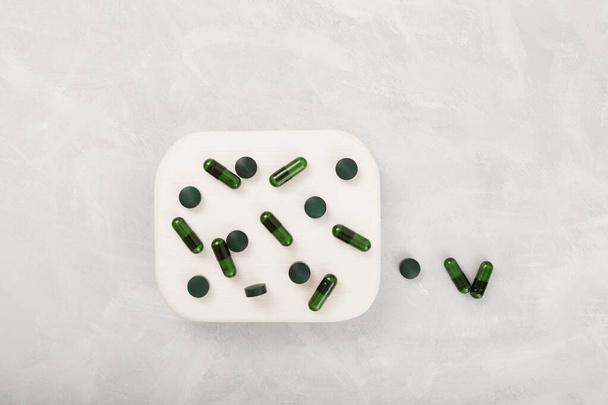 Green Capsules and Pills on white podium on grey textured background, top view. Alternative medicine concept. Healthy food supplements. - Foto, Imagem