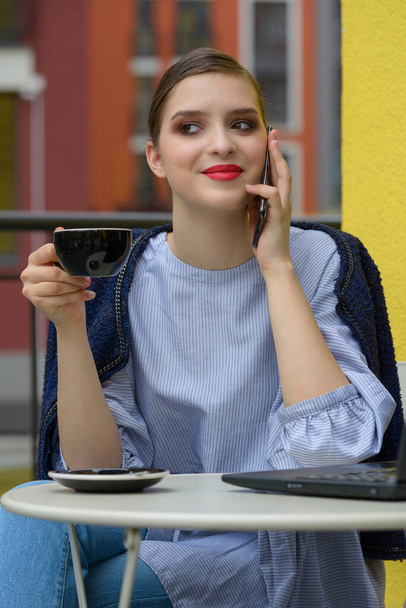 Viehättävä onnellinen nainen opiskelija kommunikoi puhelimitse ja käyttää kannettavaa tietokonetta valmistautua kurssin työtä. - Valokuva, kuva