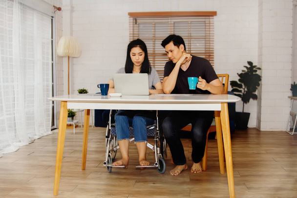 Liebeskonzept eines körperlich behinderten Paares: Behinderte Frau sitzt im Rollstuhl, arbeitet mit ihrem Freund im Wohnzimmer, pflegt und verwöhnt gemeinsam. - Foto, Bild