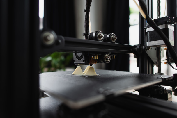 vista ravvicinata della stampante 3D che crea un modello in plastica vicino alla figura prodotta sul tavolo in un ufficio moderno - Foto, immagini